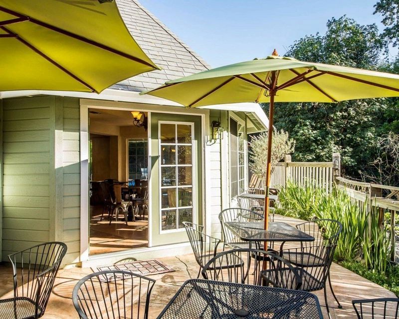 Outdoor cafe with tables, chairs, and yellow umbrellas on a wooden deck next to a building with glass doors.