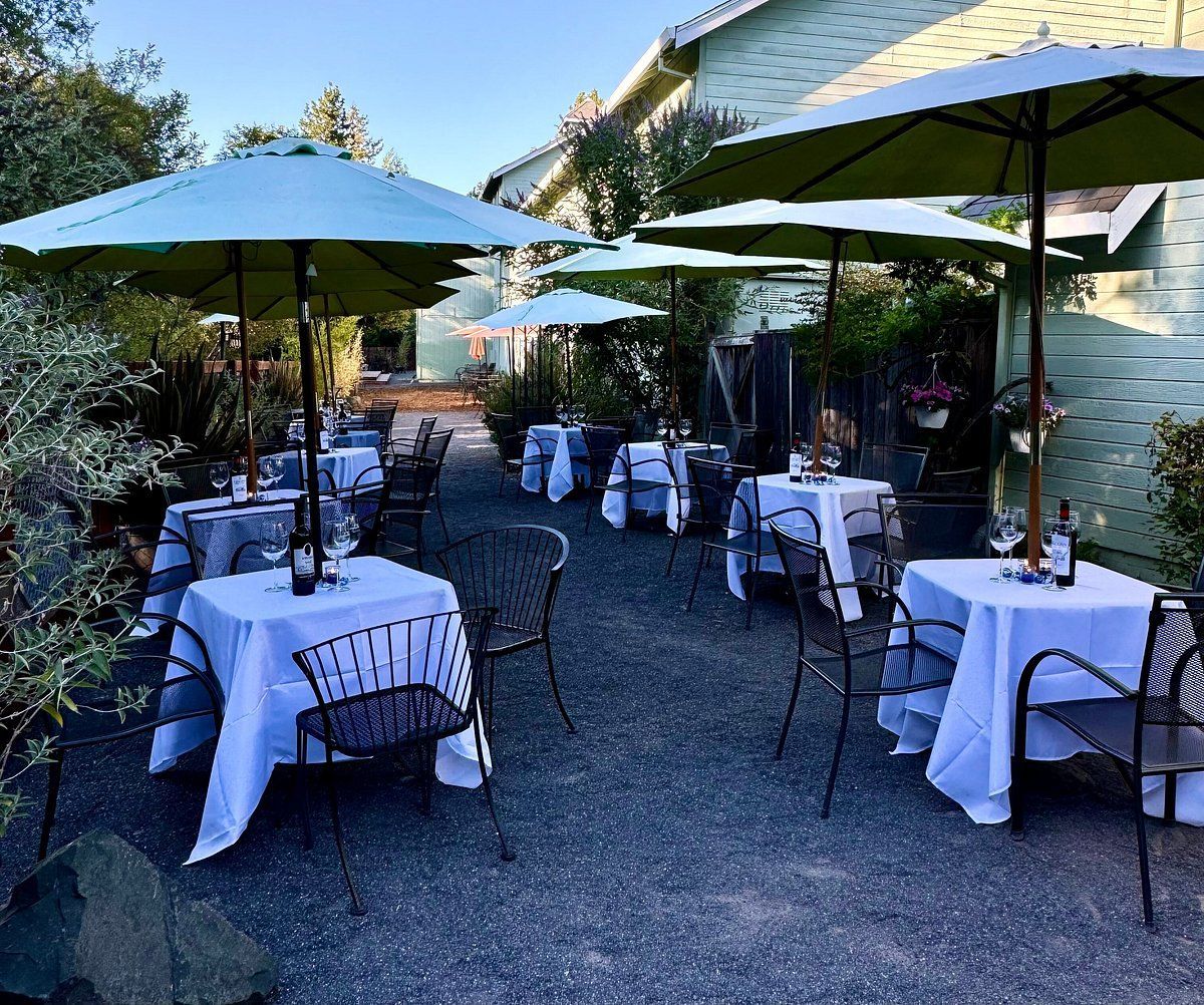 Outdoor restaurant seating with white tablecloths, under green umbrellas, in a gravel area.