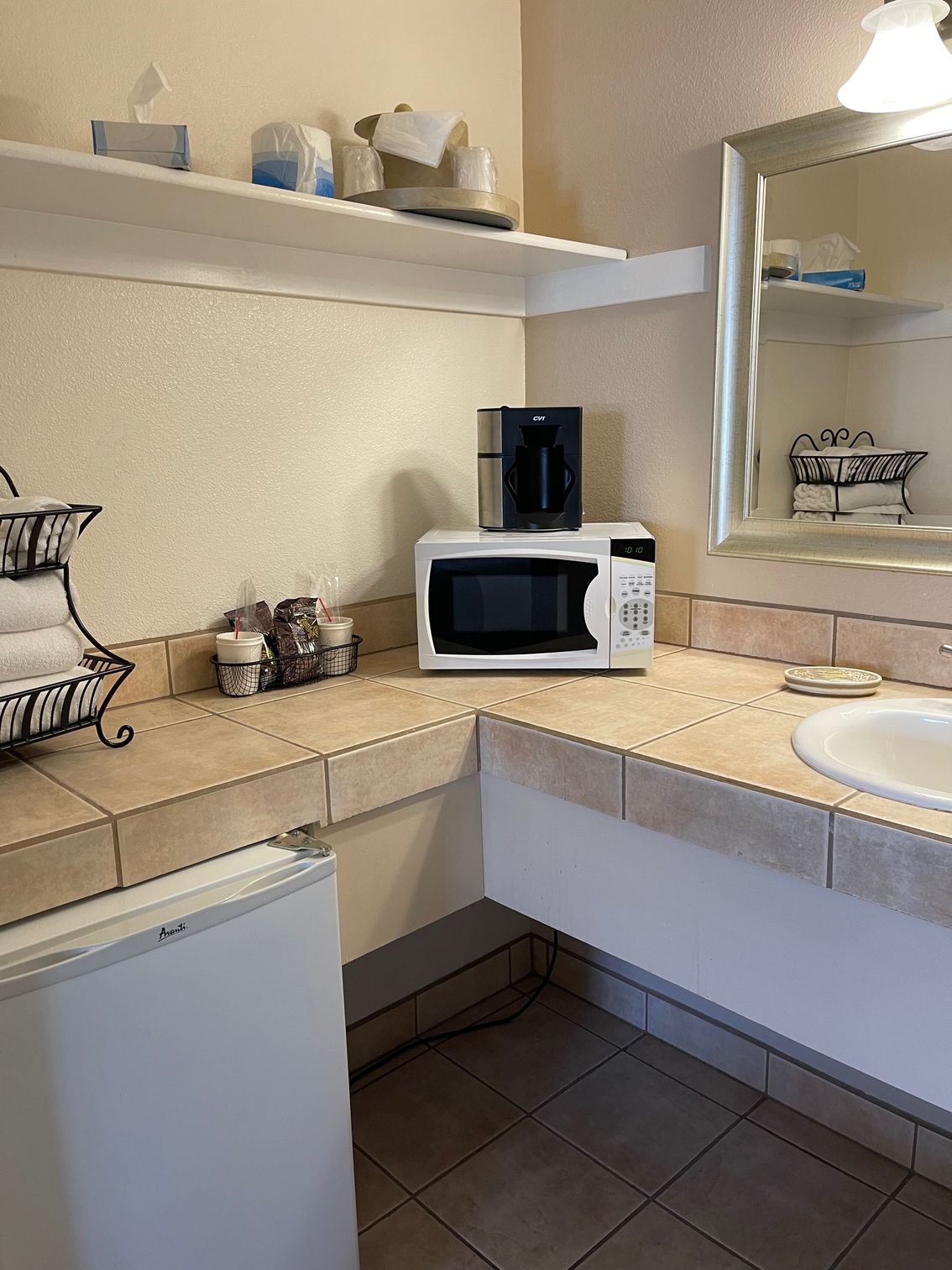 Bathroom counter with microwave, coffee maker, small fridge, and sink. White and tan colors.