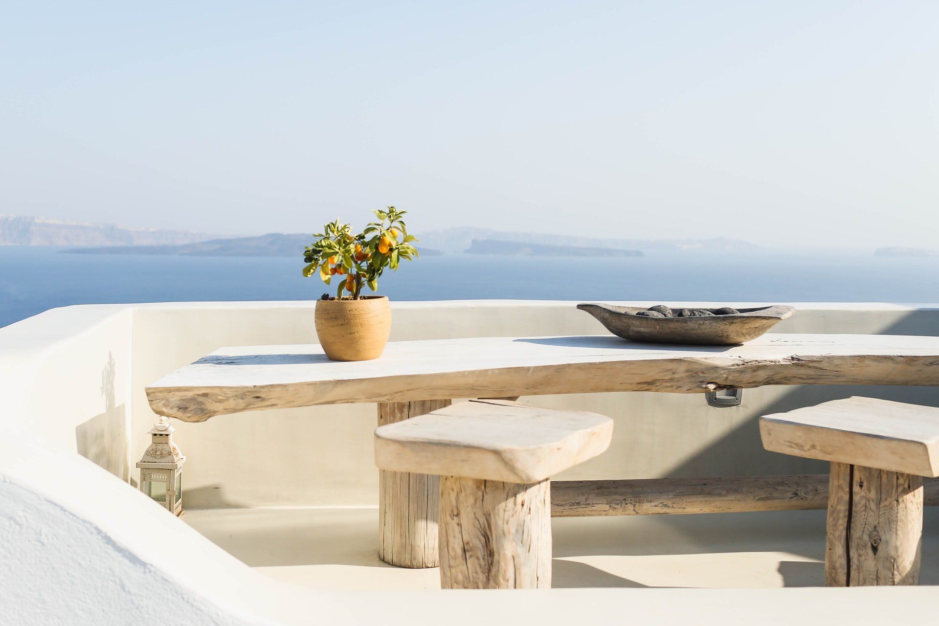 Wooden table and stools with a potted plant and bowl overlooking the sea.