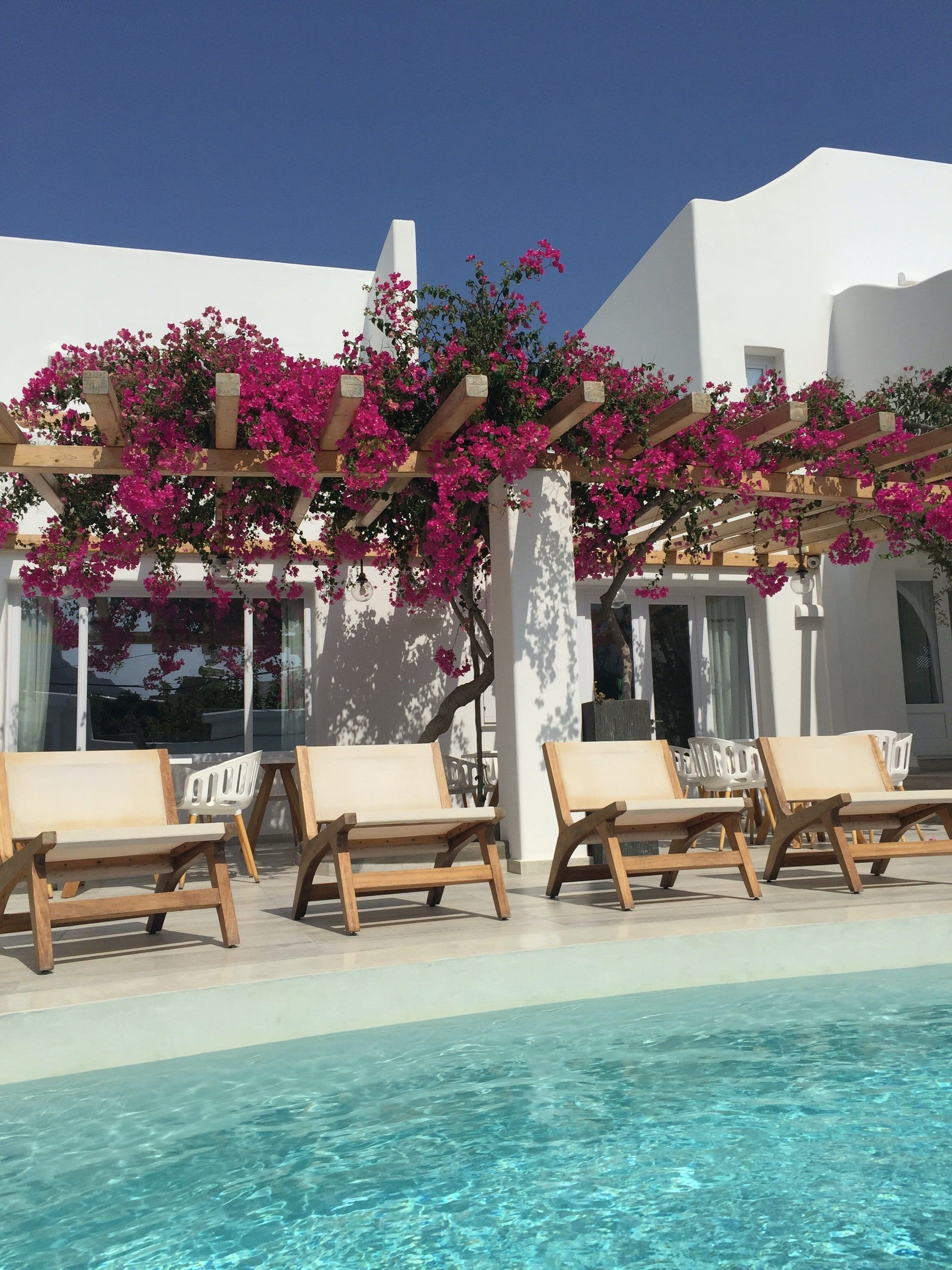 Poolside seating area with bougainvillea and white buildings.