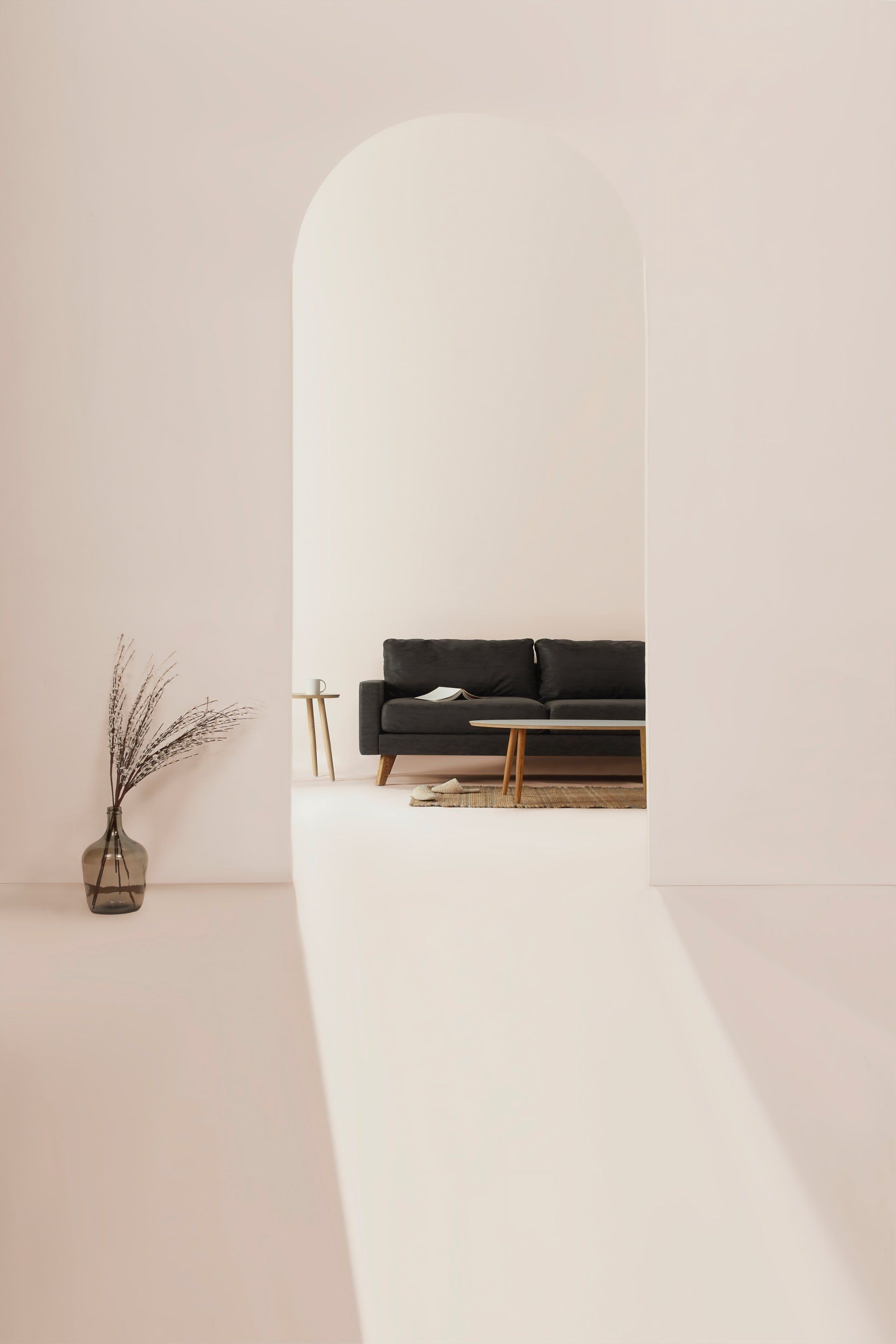 Archway to a minimalist living room with a dark sofa, coffee table, and vase of branches.