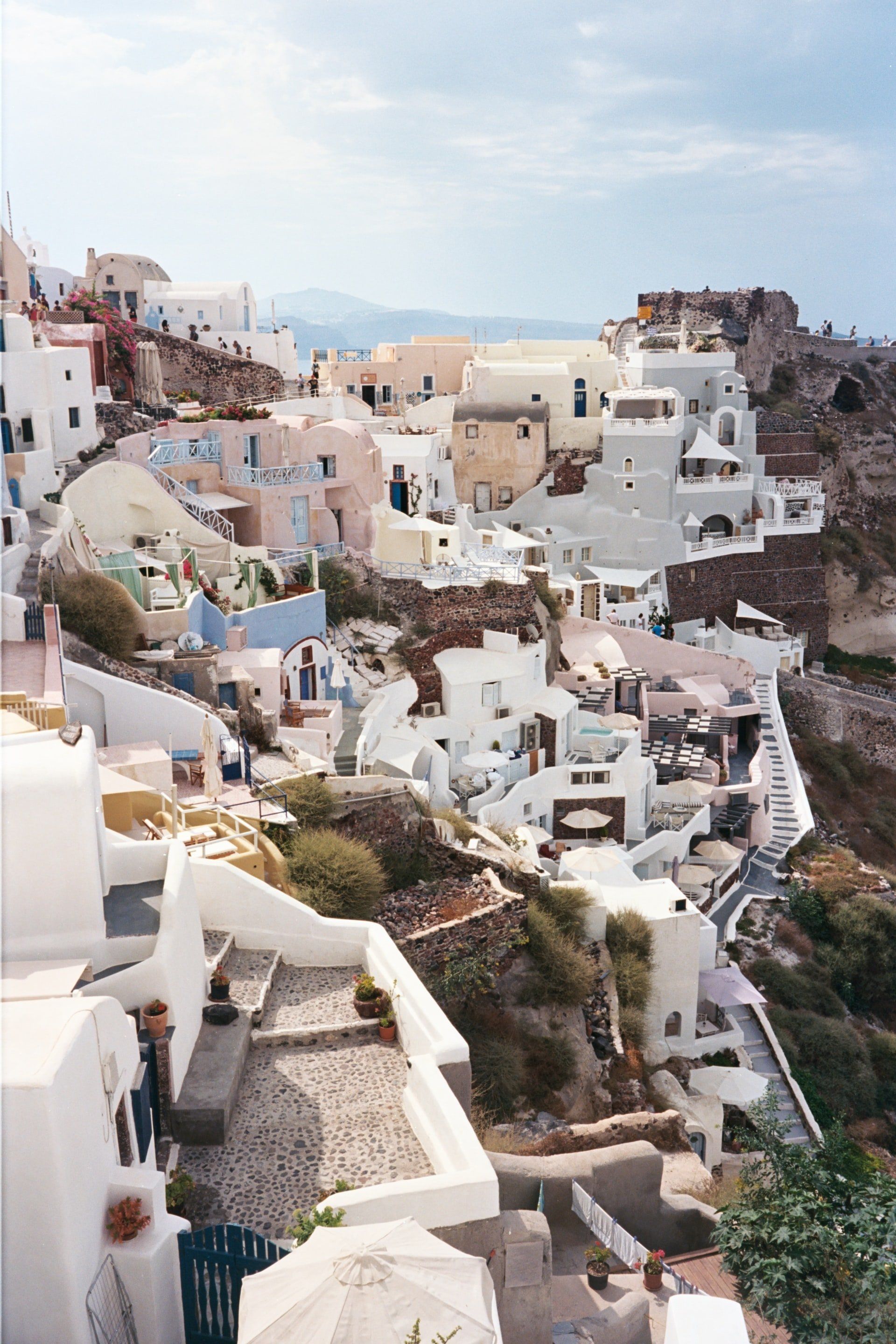 Whitewashed buildings cascading down a cliffside in Santorini, Greece; blue domes and accents against the blue sky.