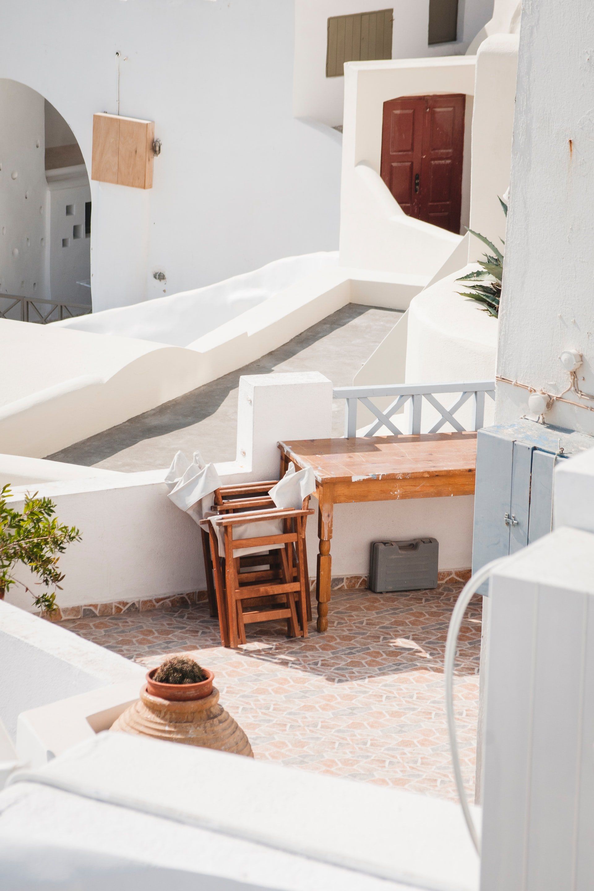 White buildings with a wooden table and chairs on a patio; Santorini, Greece.