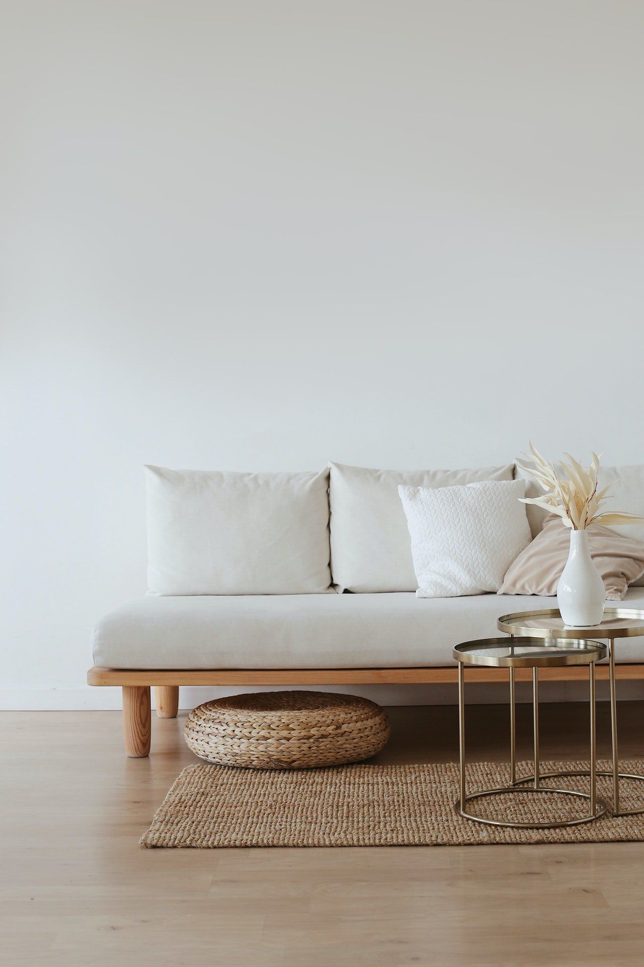 Off-white couch against a white wall with pillows, wicker basket, rug, and small gold table.