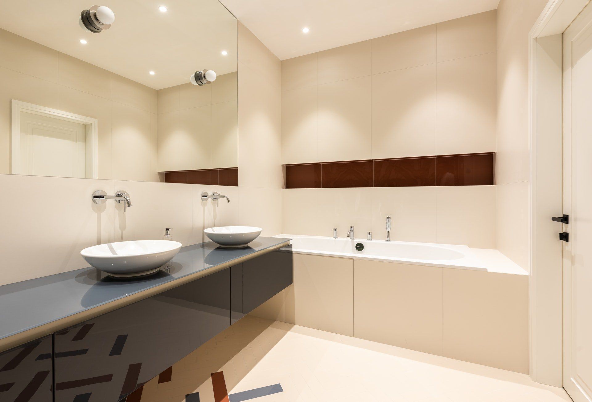 Modern bathroom with a bathtub, two sinks, large mirror, and brown accent tile.