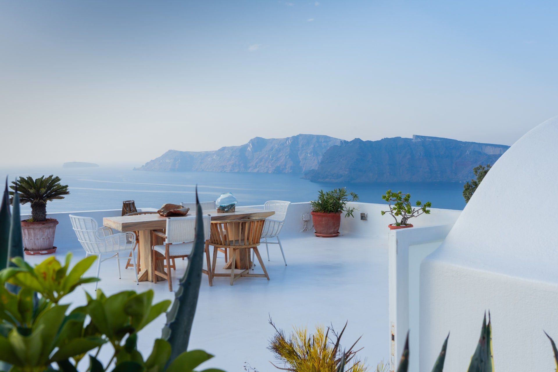Outdoor dining area overlooking the Aegean Sea, white architecture with plants and furniture.