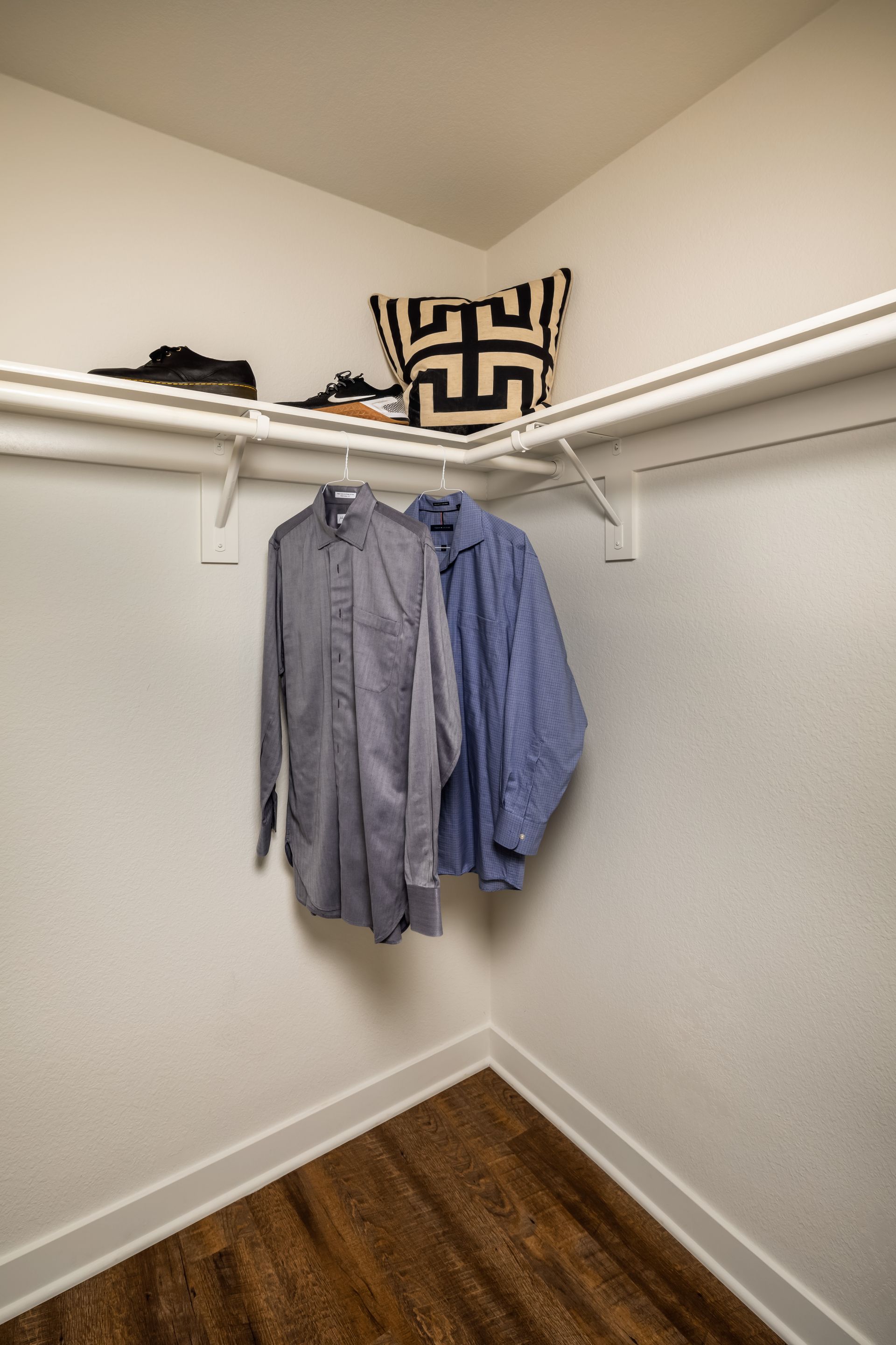 A closet with shirts hanging on a rack and a pillow on the ceiling.