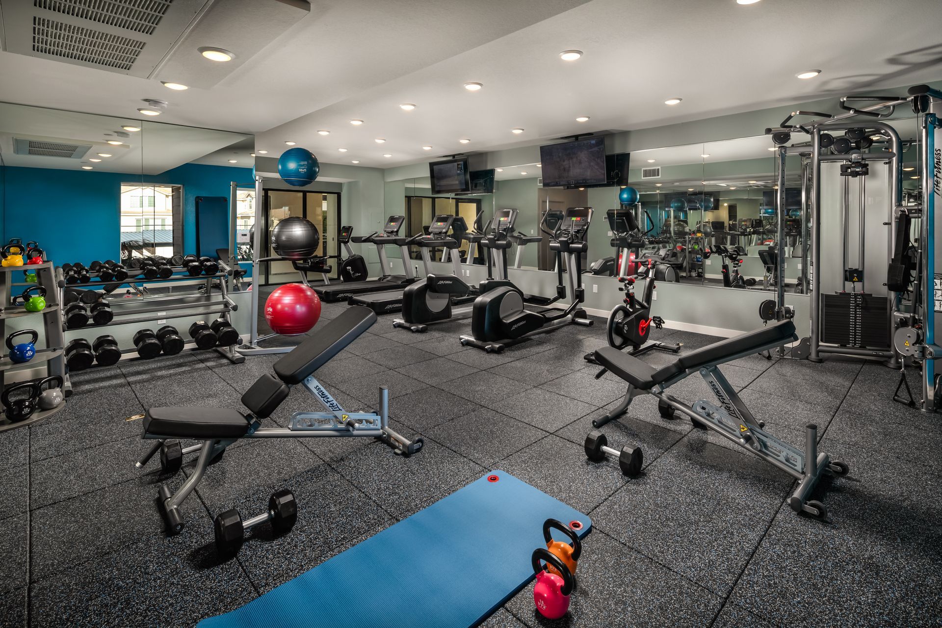 A large gym filled with lots of exercise equipment and a yoga mat.