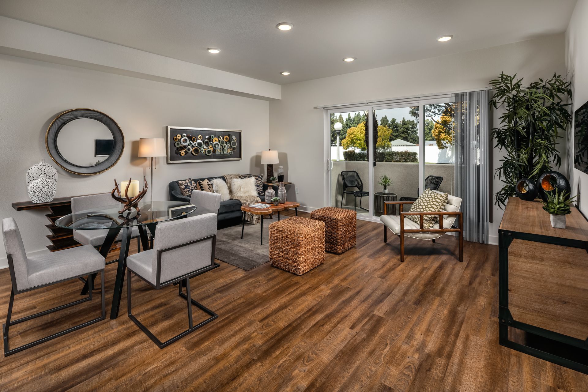 A living room with hardwood floors , a couch , chairs , a table and a sliding glass door.