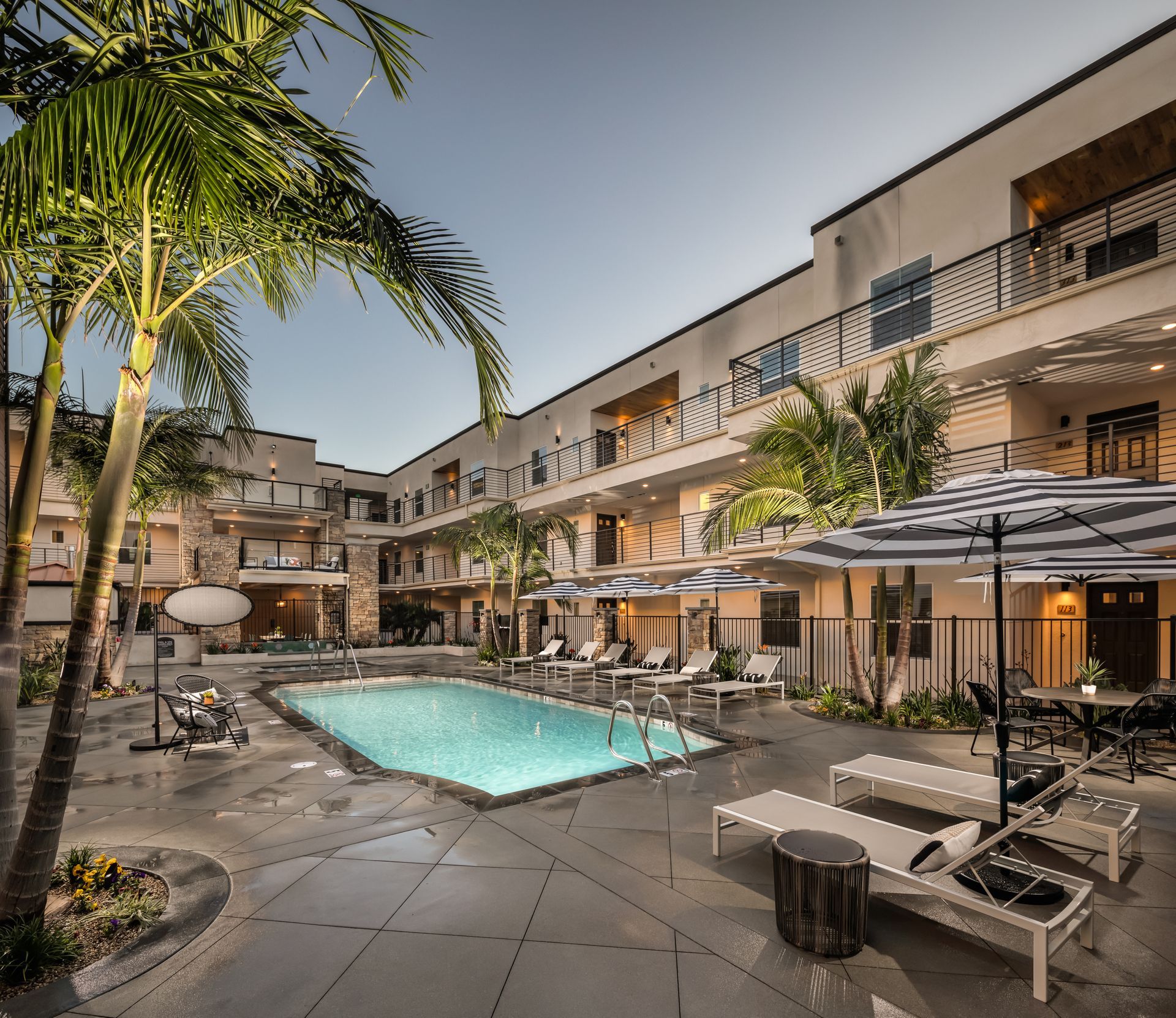 A large swimming pool surrounded by lounge chairs and umbrellas in front of a hotel.