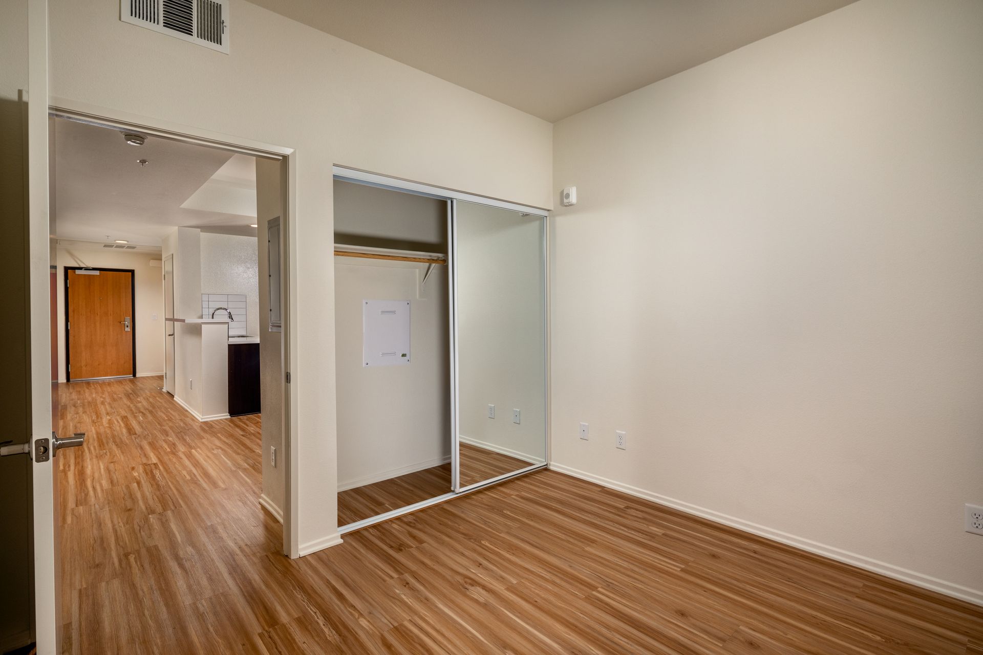 An empty bedroom with hardwood floors and a closet with sliding glass doors.
