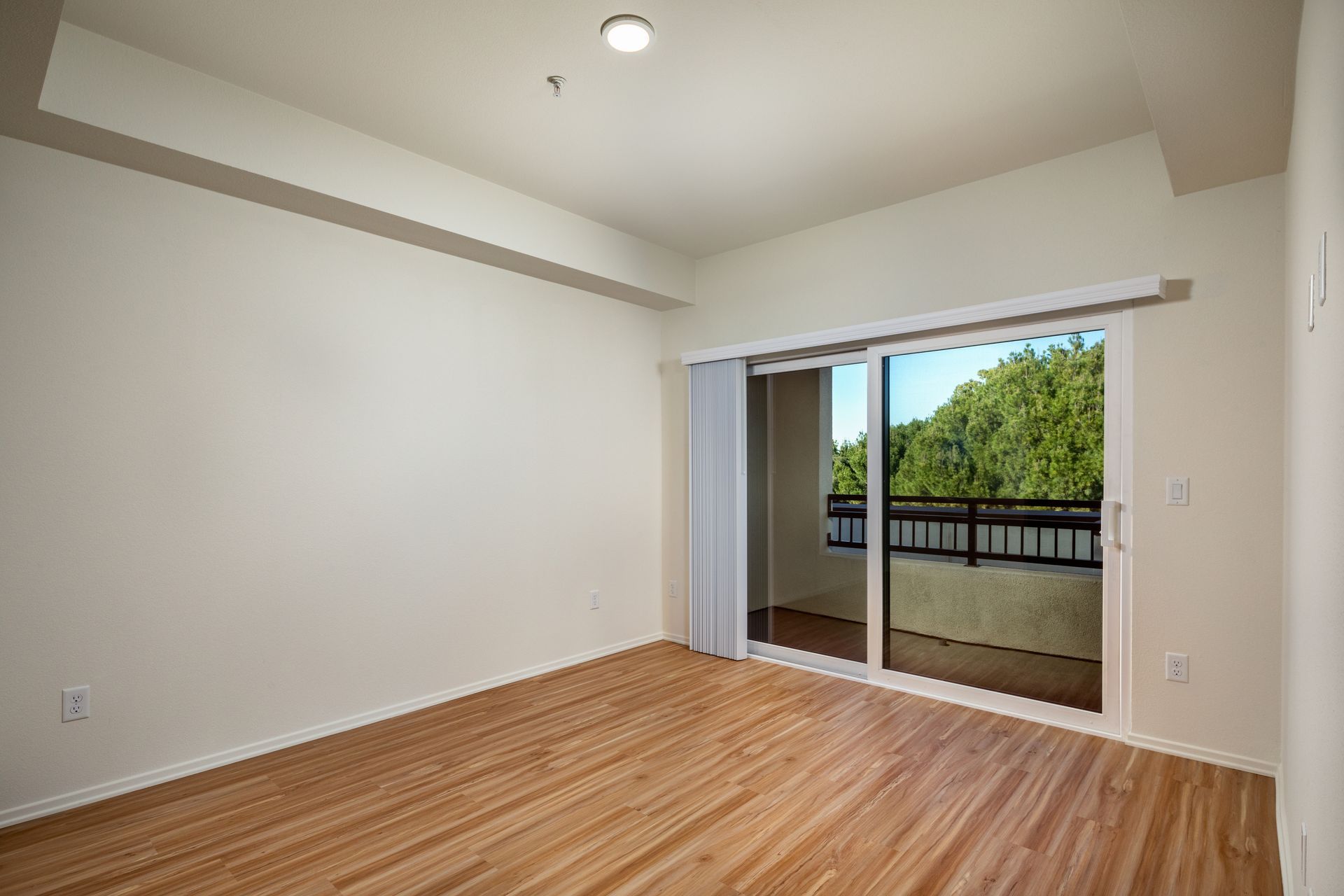 An empty living room with hardwood floors and sliding glass doors leading to a balcony.