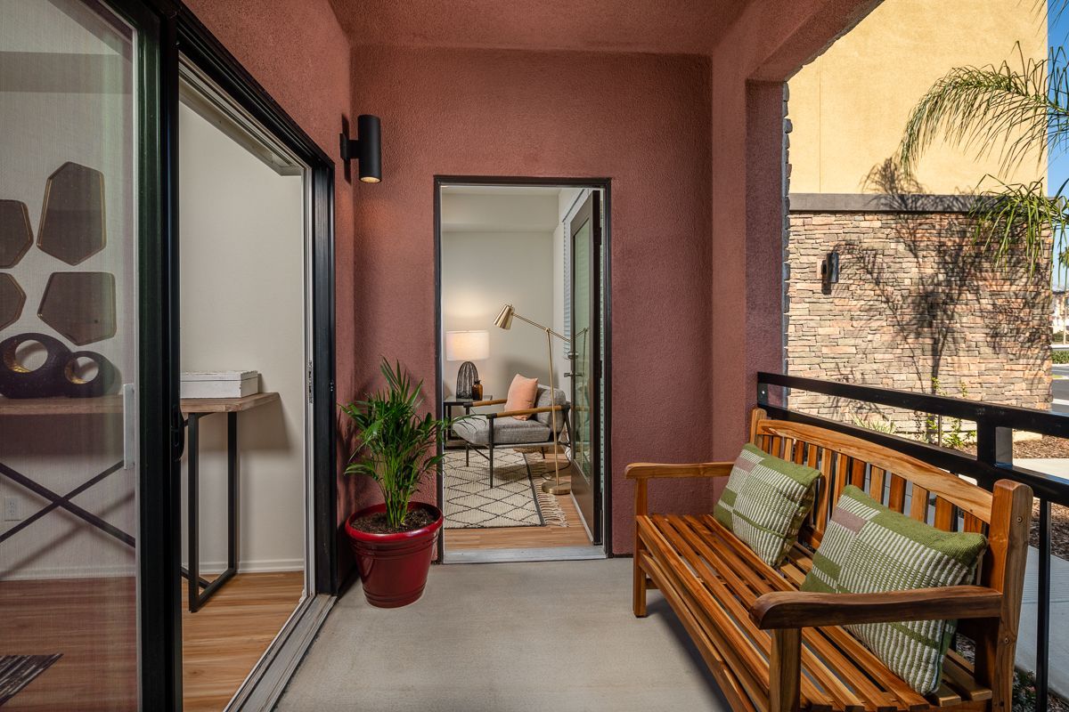 A balcony with a wooden bench and sliding glass doors leading to a living room.