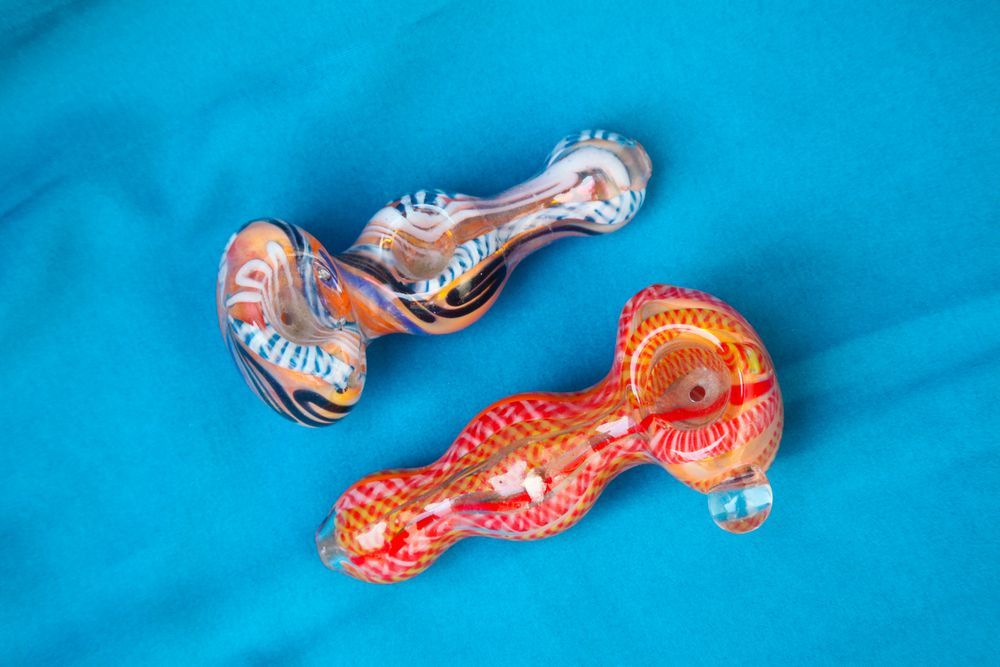 Two colorful glass pipes are sitting on a blue surface.