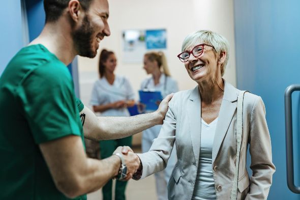 A nurse is shaking hands with an older woman in a hospital hallway.