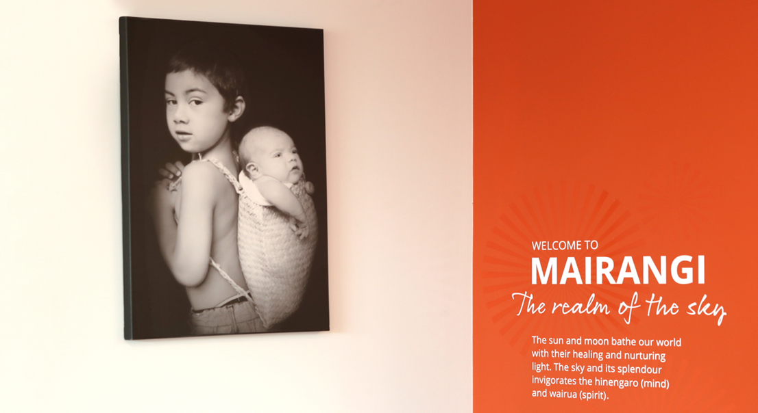 A black and white photo of a child carrying a baby is hanging on a wall.