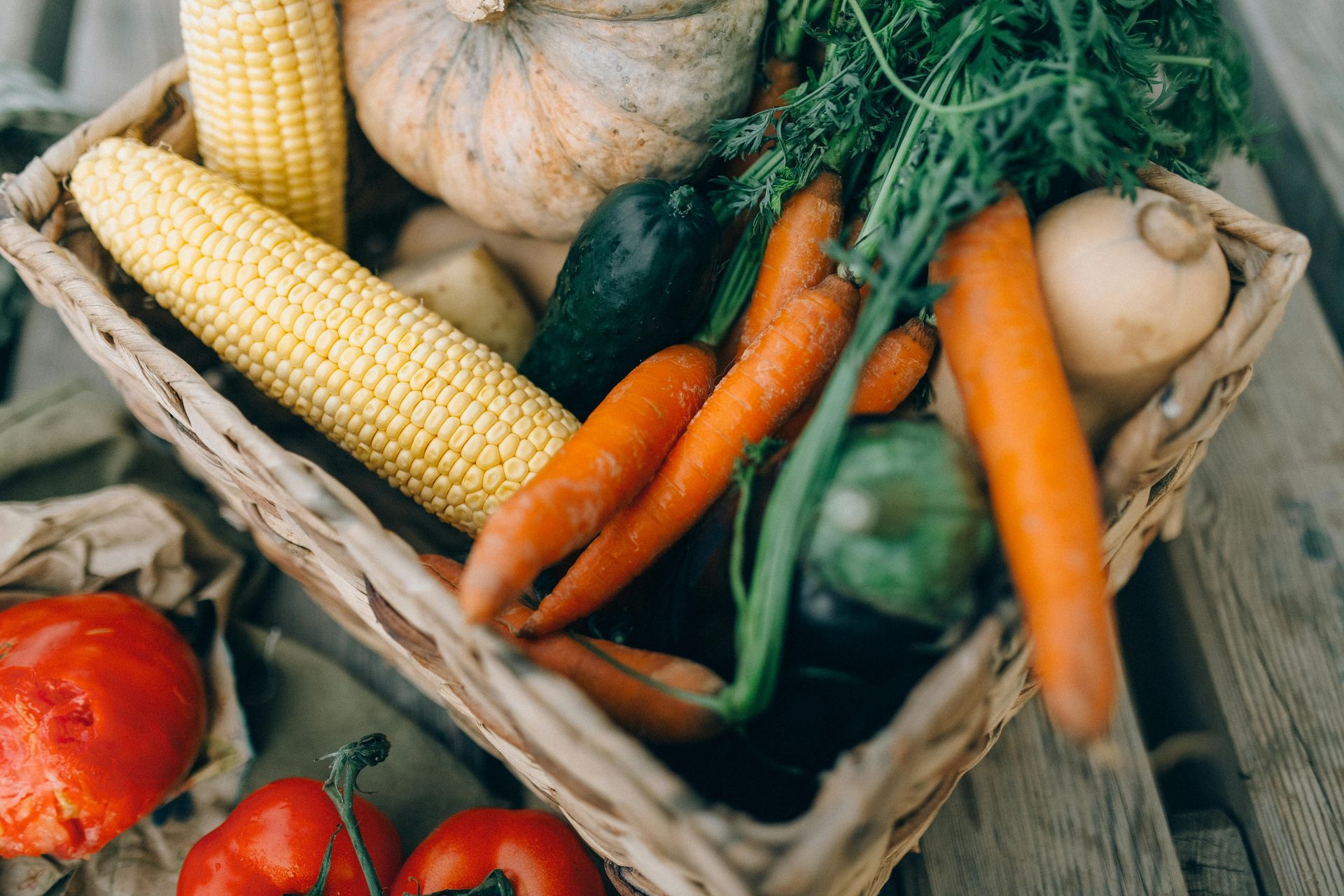 Un panier tressé rempli de produits frais, notamment du maïs, des carottes, une citrouille et des légumes à feuilles