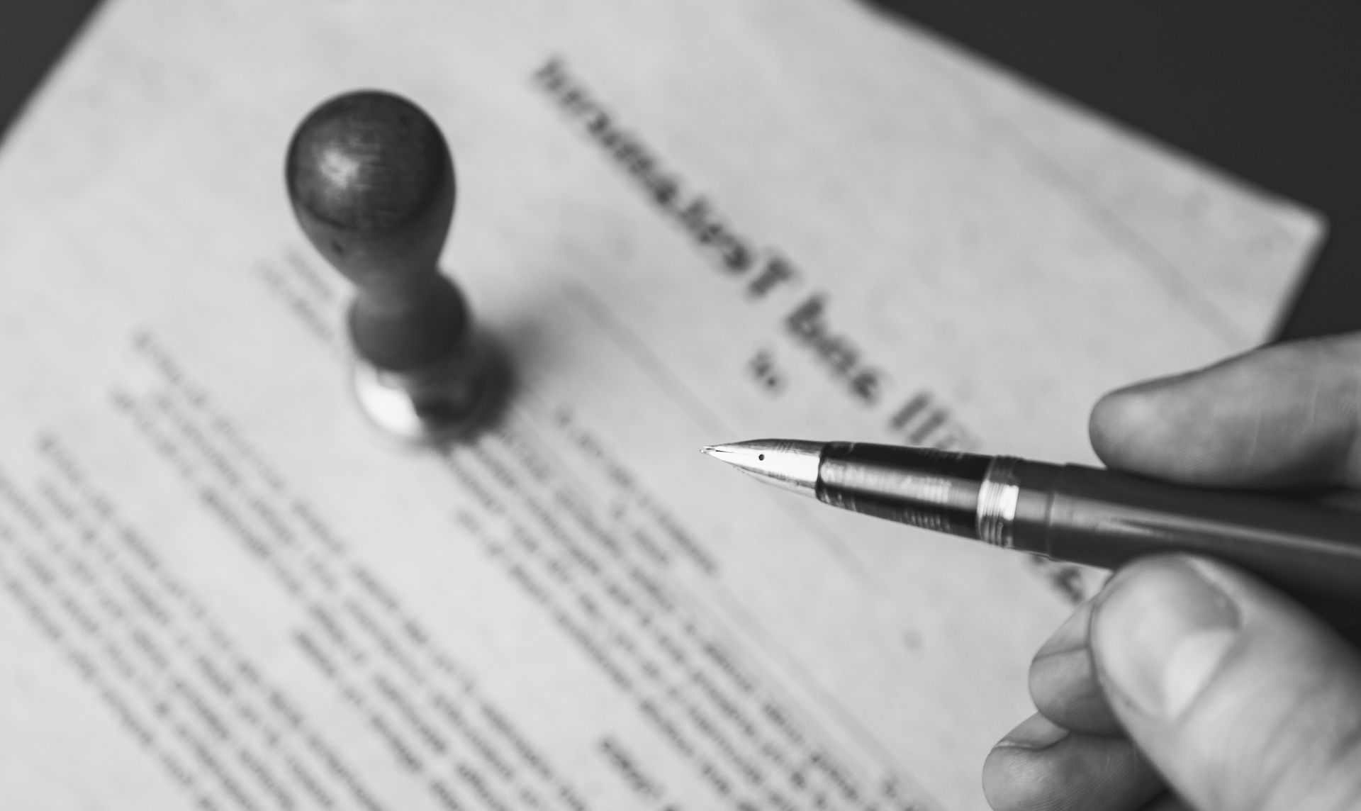 Hand signing a document with a pen beside a stamped page