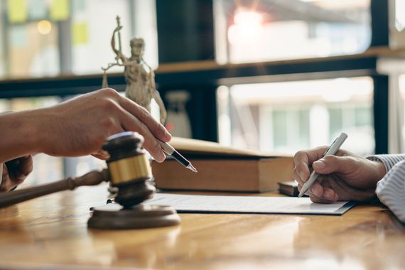 Two people signing legal documents beside a judge’s gavel on a wooden table