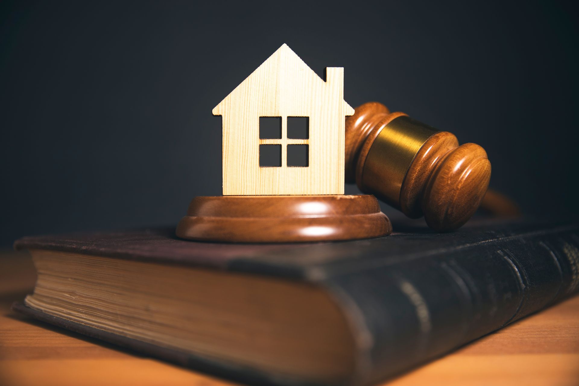 Wooden house model on a gavel atop law books, symbolizing real estate law.