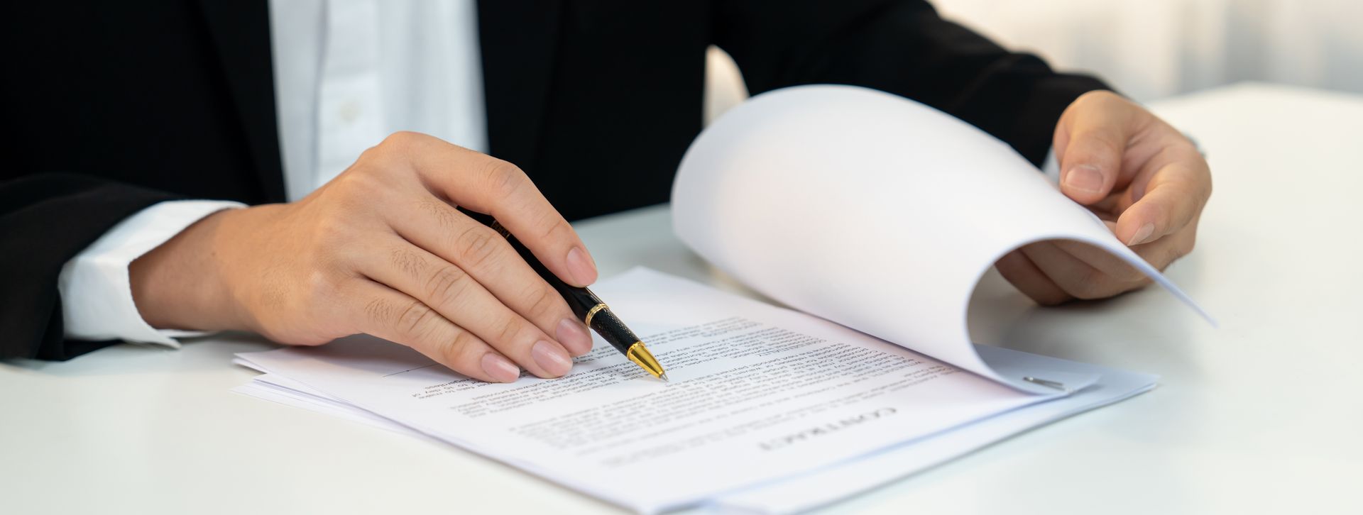 Hands in a suit signing a document with a pen on a desk.