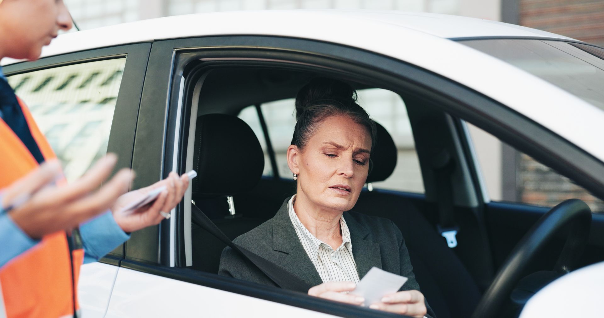 Woman sitting in driver’s seat of a white car, looking down at papers handed through the window