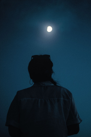 Person seen from behind looking up at a bright moon in a dark blue night sky