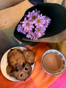 Flowers in a black vase beside a plate of muffins and a cup of tea on an orange cloth