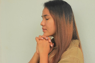 Profile of a woman with hands clasped under her chin, eyes closed, against a plain light background