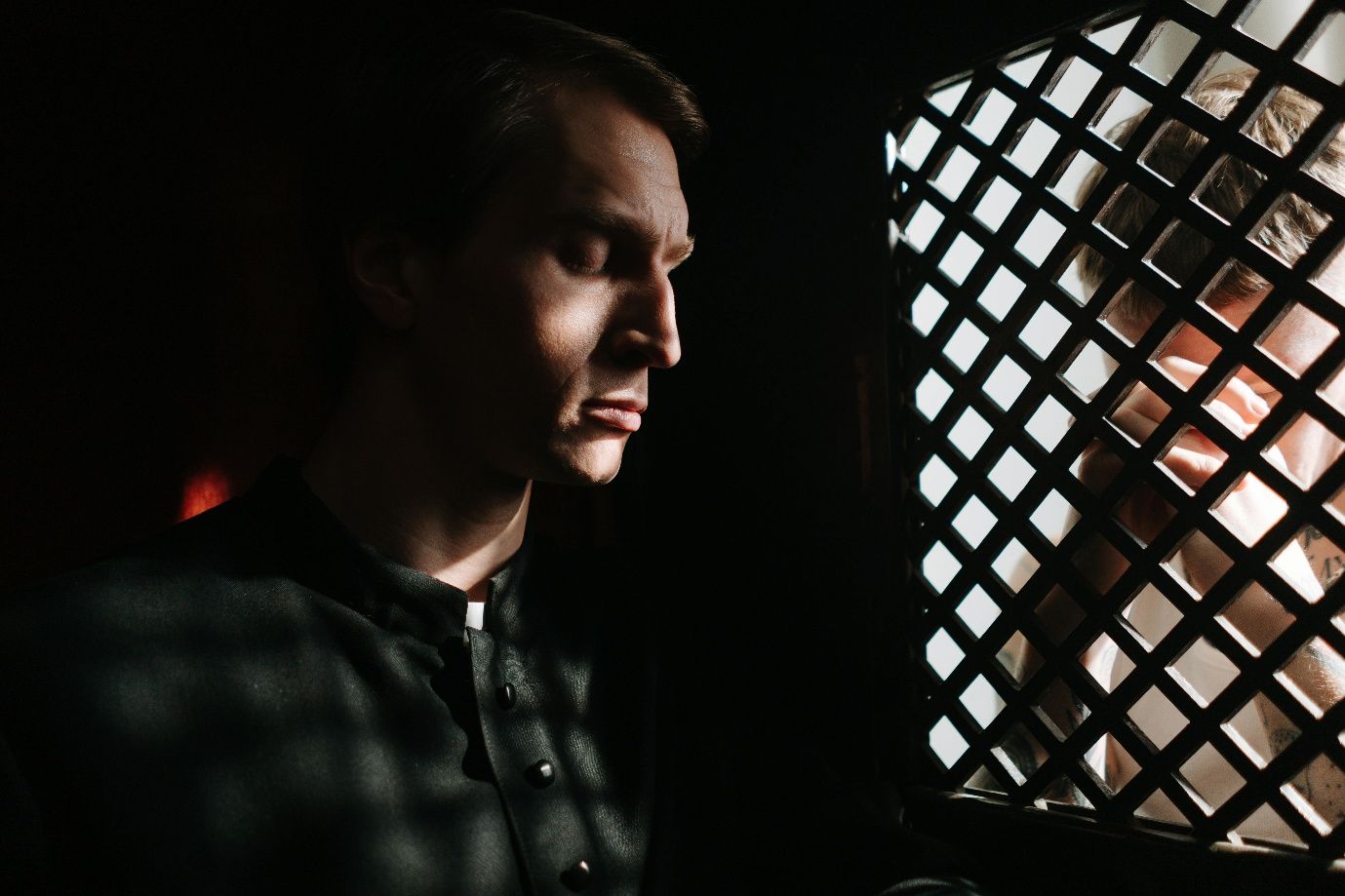 A priest in a confessional with a penitent behind a grill