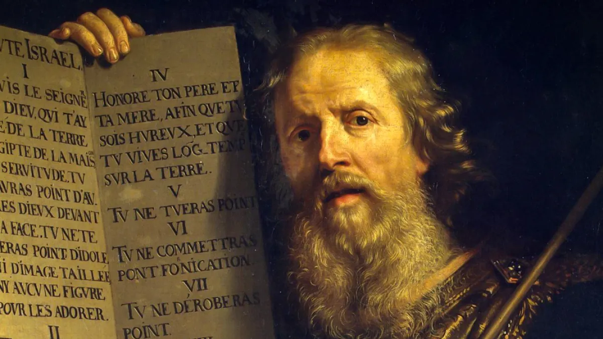 Bearded man holding an ancient scroll with Latin text, lit by warm light.
