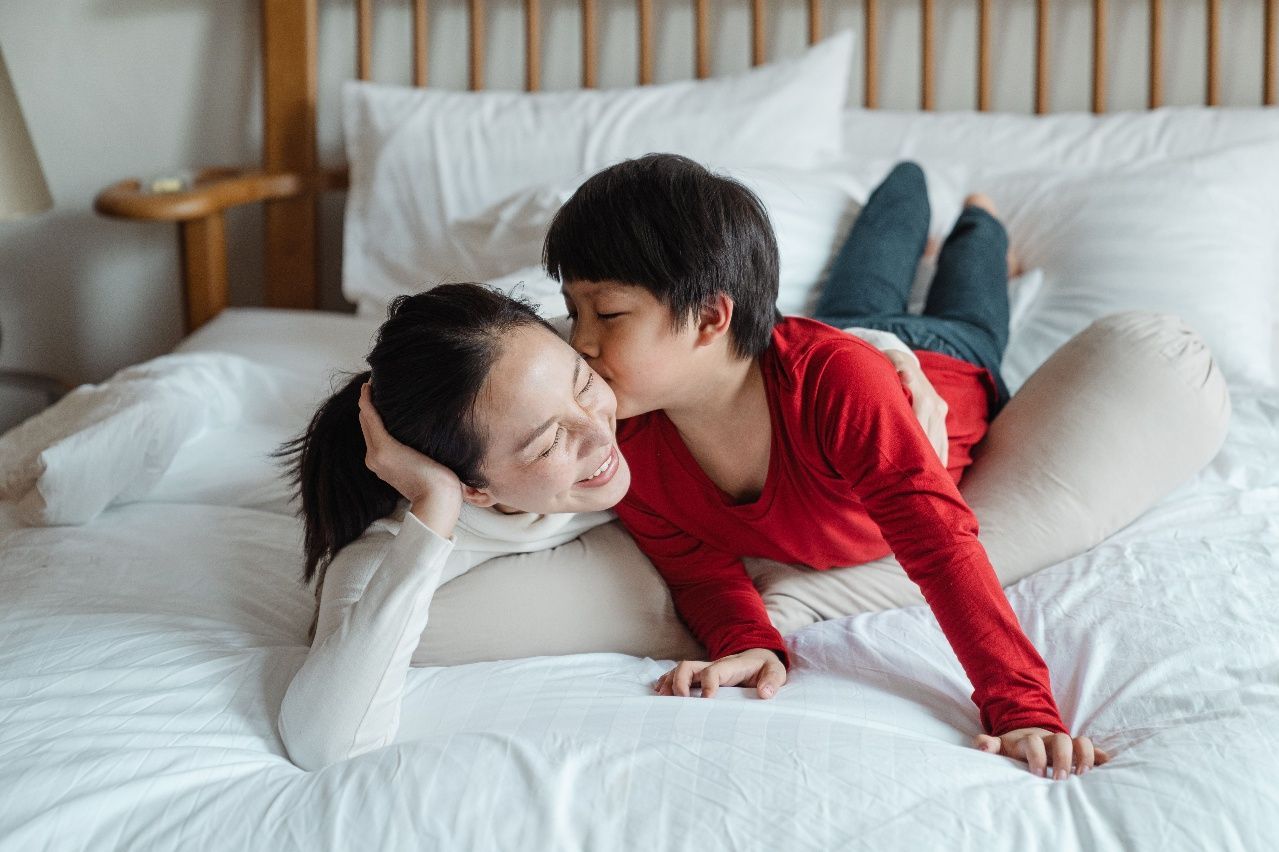 Two people lying on a bed, smiling and sharing a kiss in a cozy bedroom.