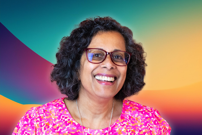 Tammy Fernando, wearing glasses and a pink shirt, is smiling.