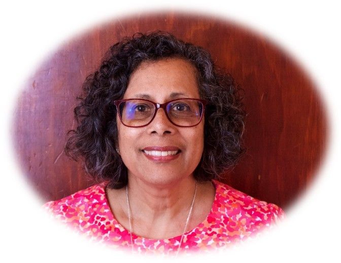 Smiling woman with glasses in a pink floral top against a wooden background