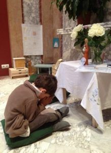 A young boy is kneeling on the floor reading a book.