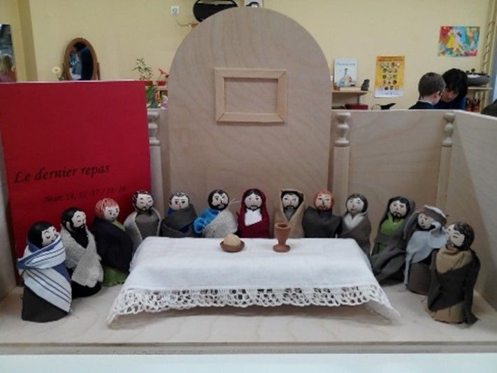 A group of dolls are sitting around a table with a book in the background that says le dernier repas
