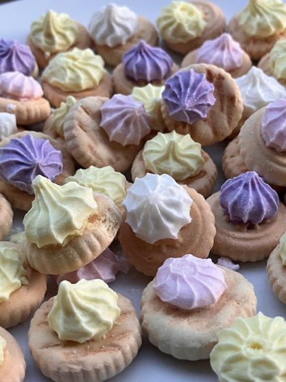Assorted mini tartlets topped with pastel whipped frosting in yellow, white, and purple colors
