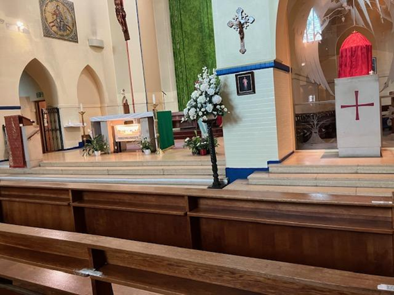 Church altar with wooden pews, white flowers, and a red-draped lectern beside a crucifix and candles