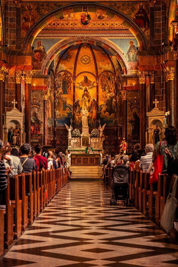 Ornate church interior with pews, patterned floor, and altar at the far end, lit in warm gold tones