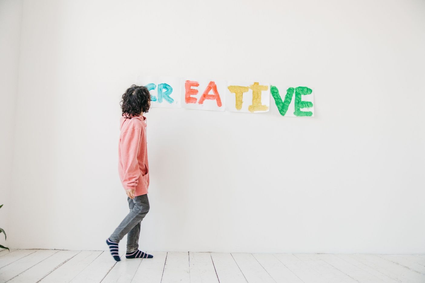 Child walking toward colorful “CREATIVE” letters on a white wall