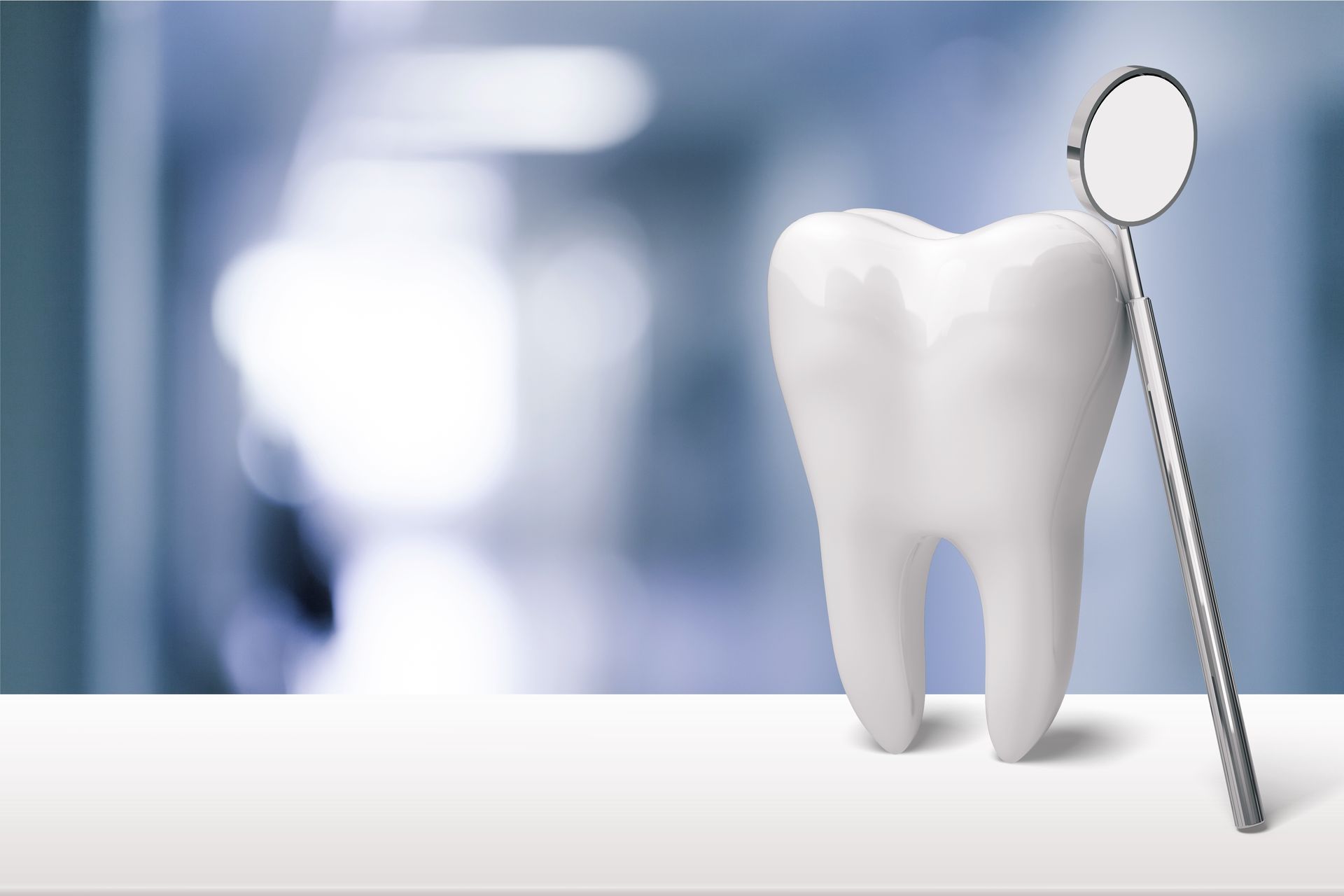 White tooth model with dental mirror in front of a blurred background.