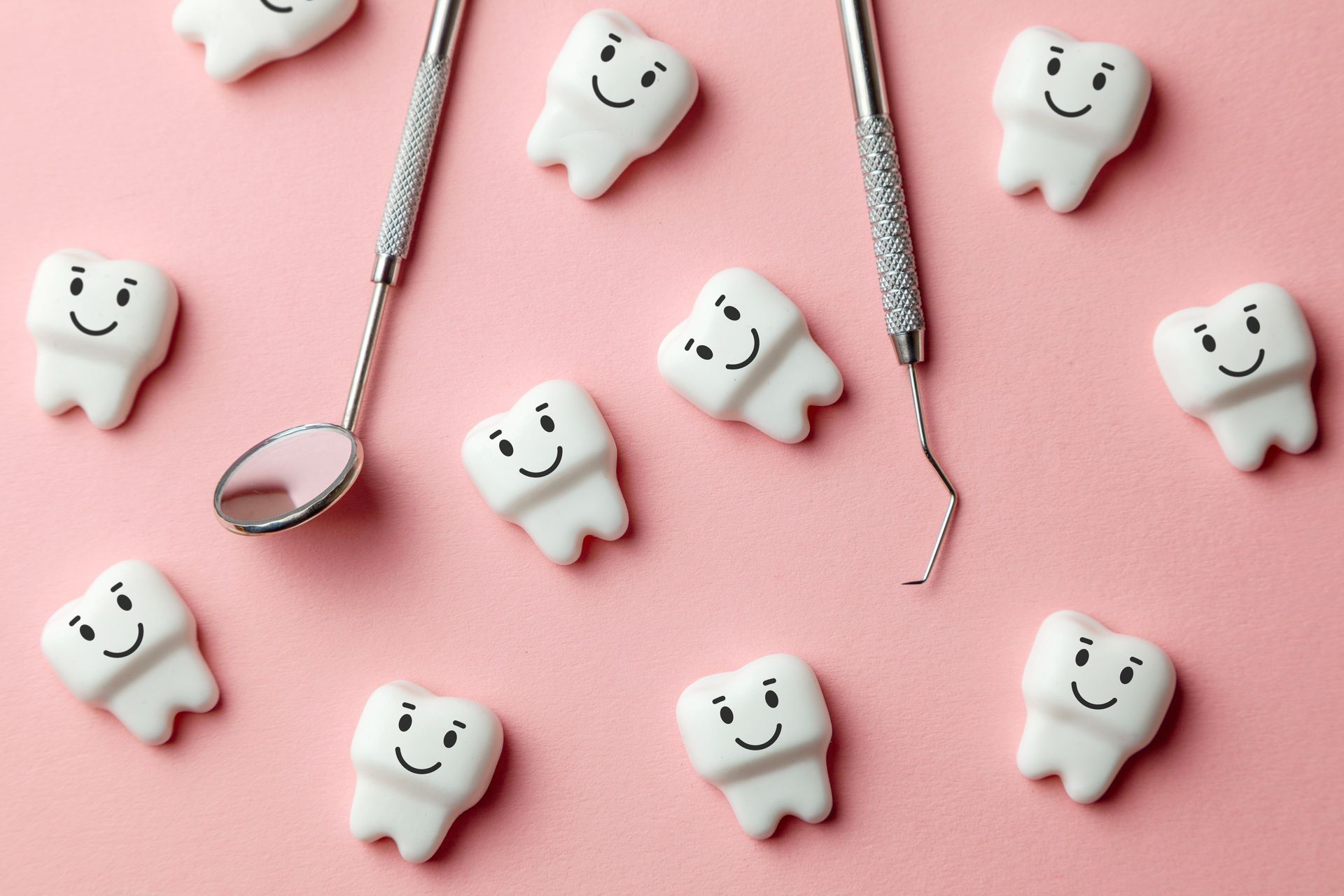 Dental tools and smiling tooth models arranged on a pink background.