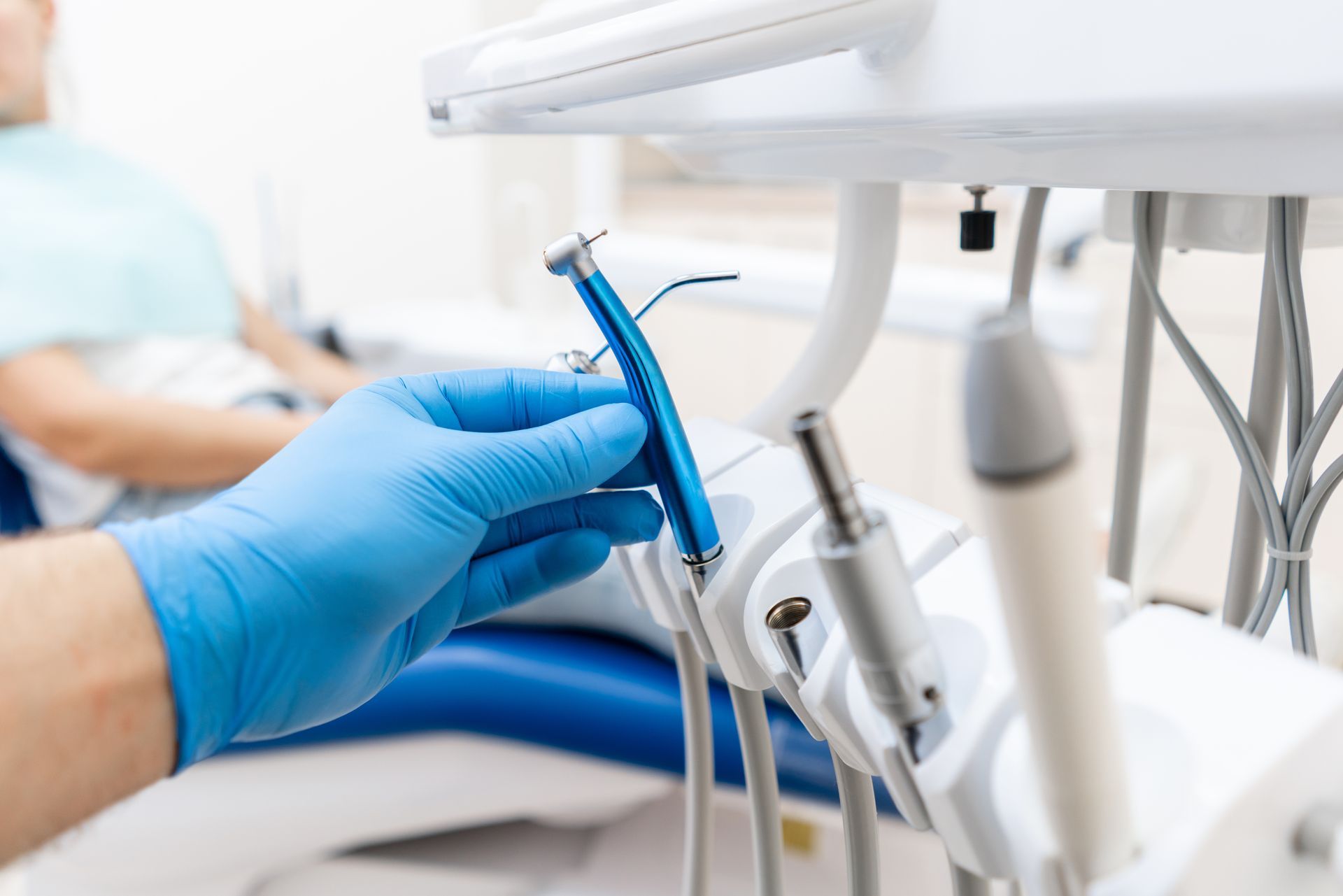 Gloved hand holding dental instrument beside a patient chair in a clinic