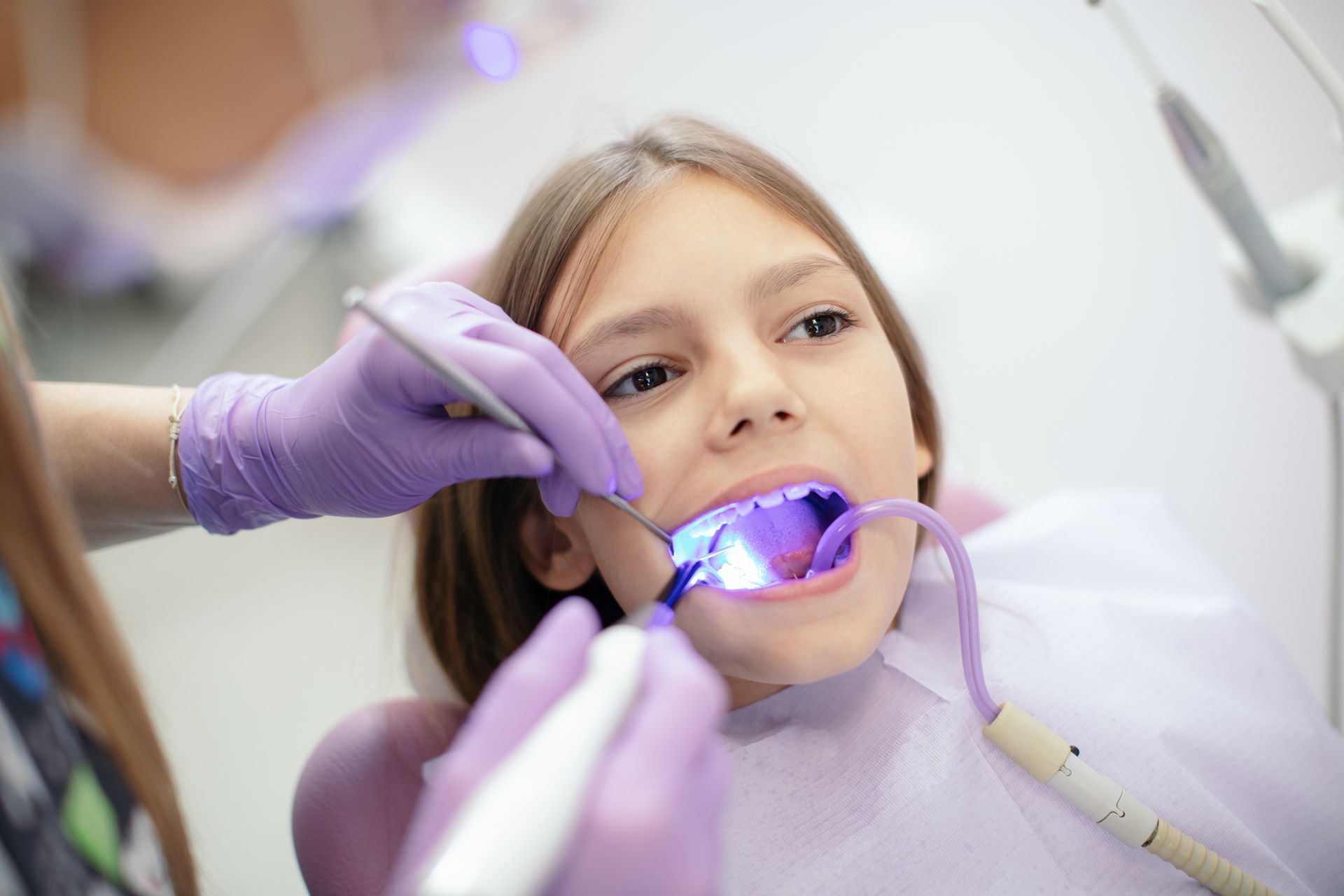 A dentist examines a young girl’s teeth during a Pediatric Airway Dental Treatment appointment. Girl in dental chair with mouth open, receiving dental treatment.