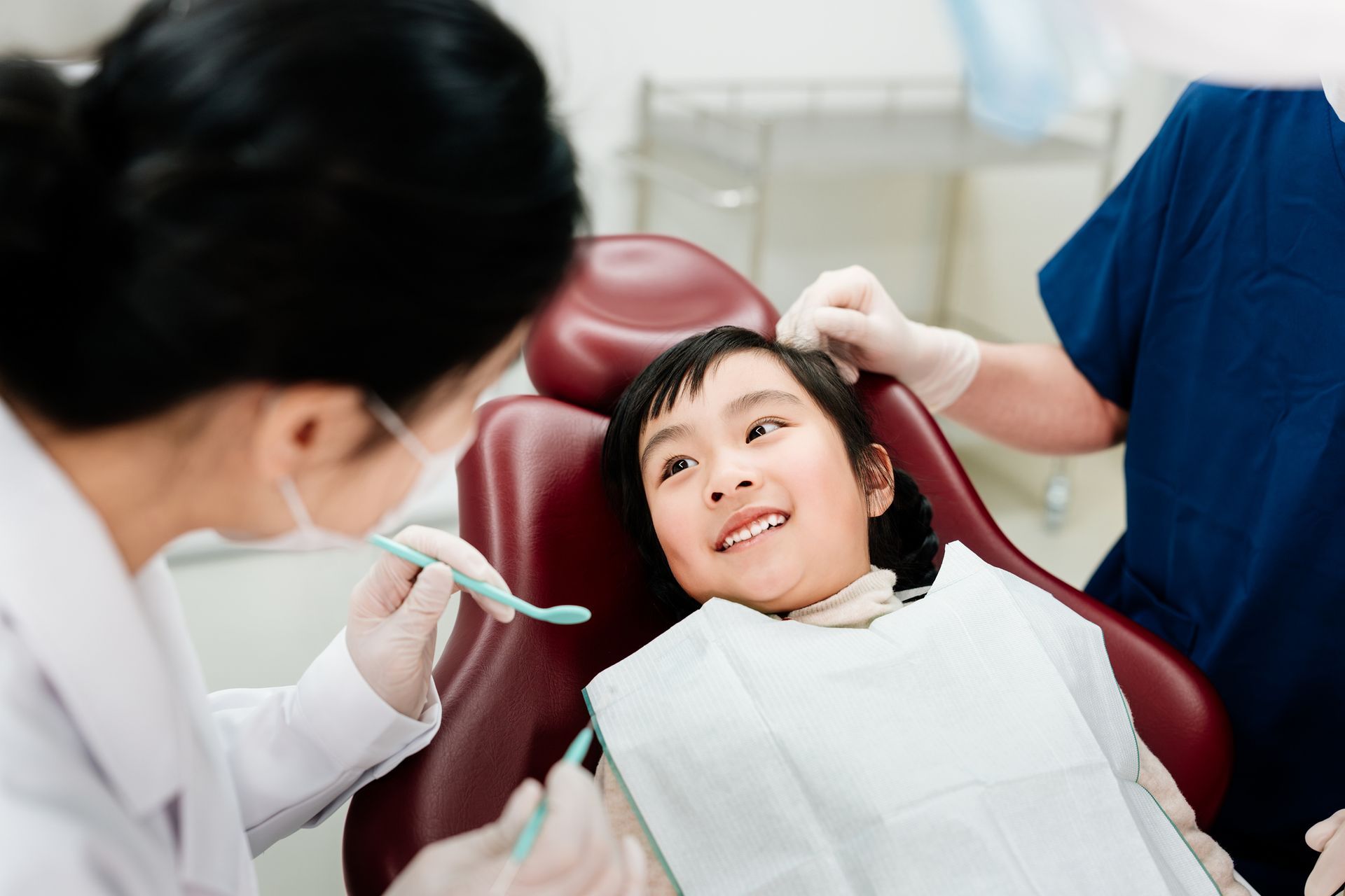 A child in a dental chair smiles as a dentist examines her mouth.