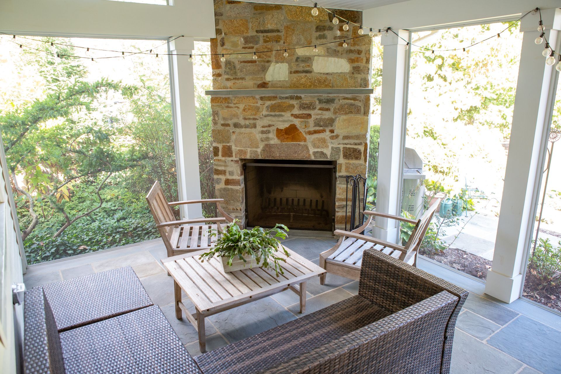 Cozy outdoor seating area with fireplace and stone facade, surrounded by greenery.