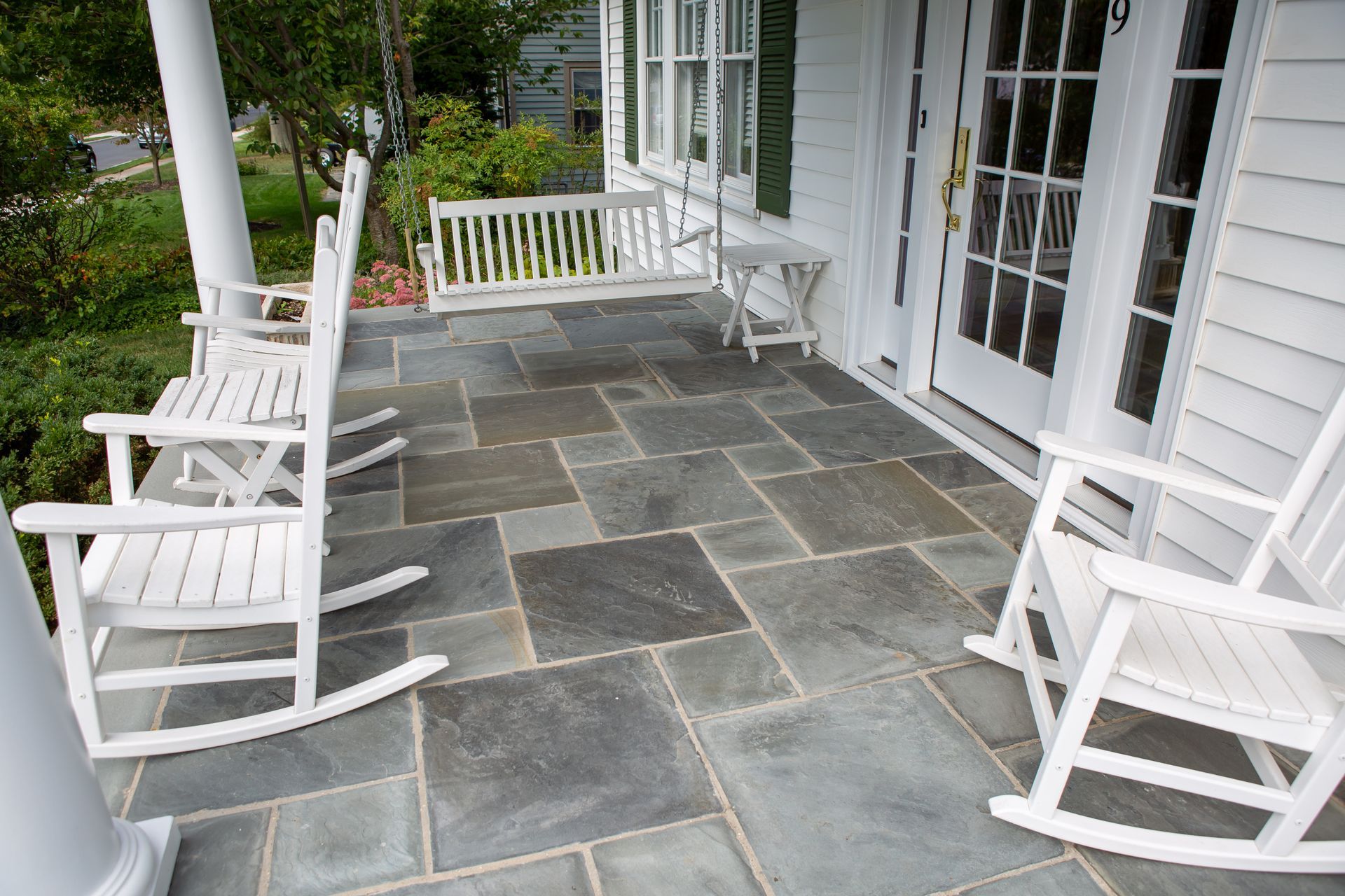 White porch with gray stone tiles, white rocking chairs, and a swing.