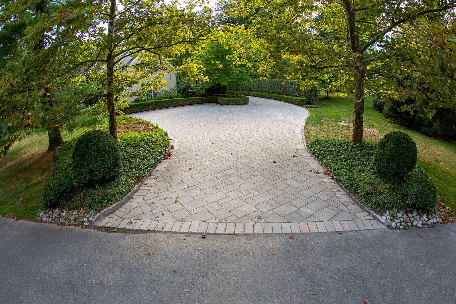 Stone driveway lined with greenery and trees, leading to a building.