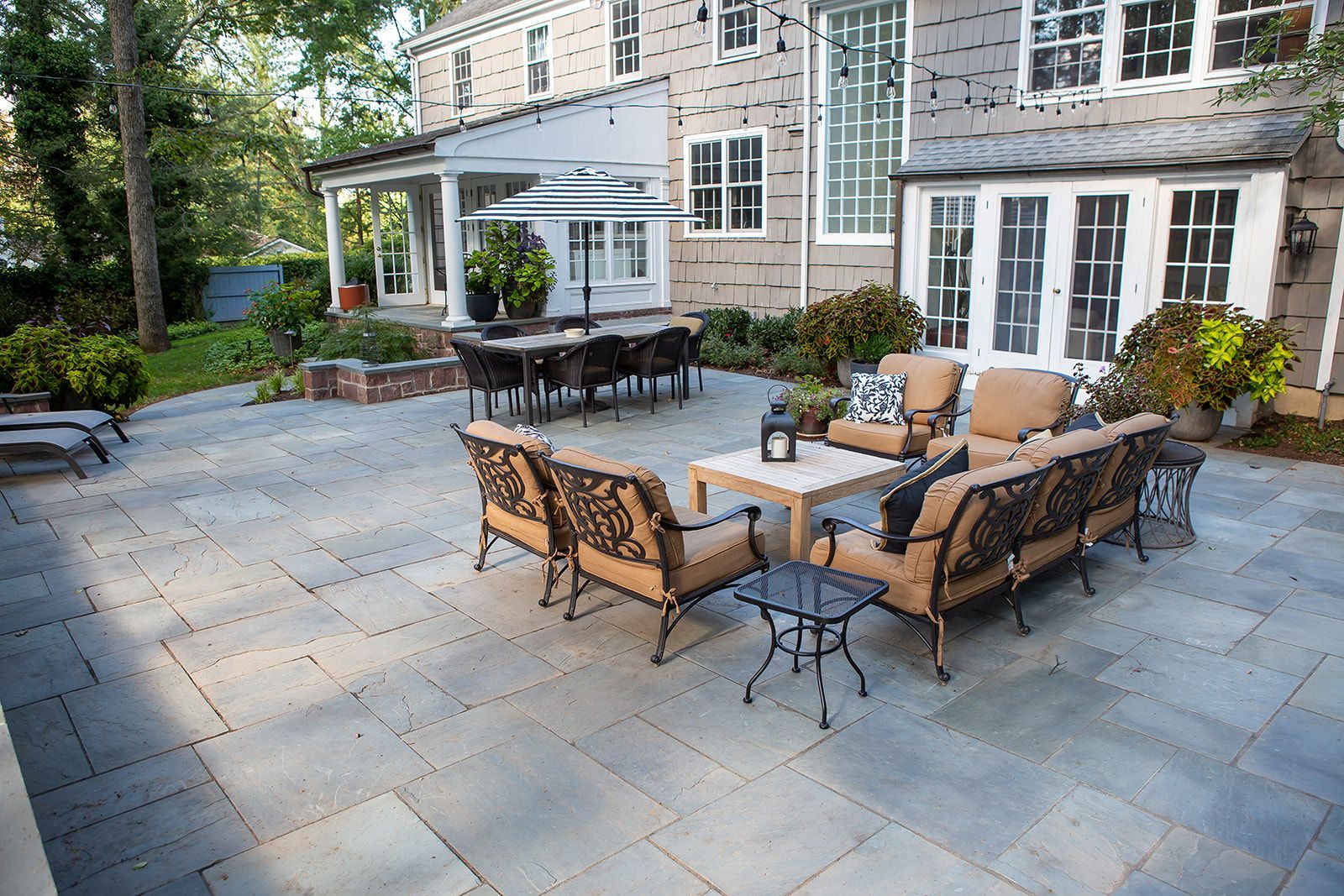 Large stone patio with outdoor furniture in front of a gray house. Dining and seating areas.